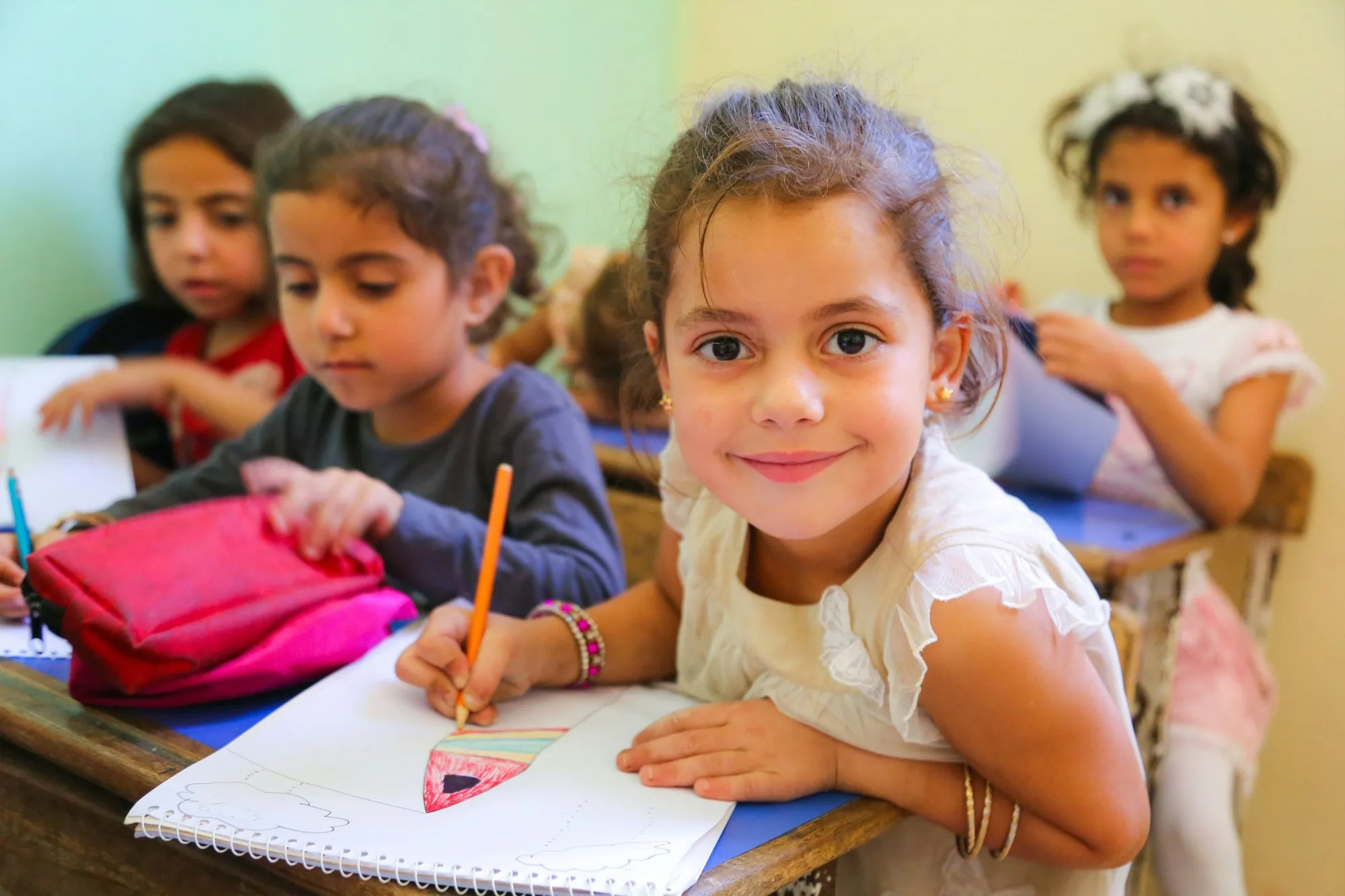 A child colouring at a table in a busy Sunshine Steps classroom