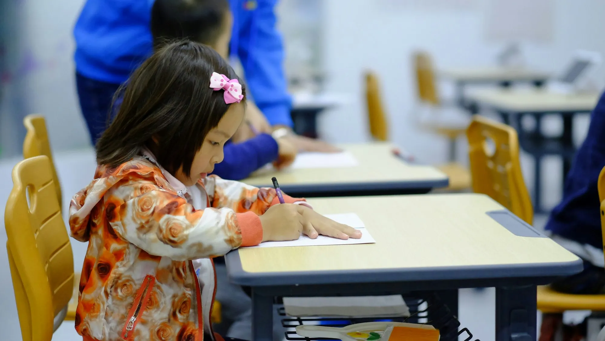 A child concentrating on writing at a classroom desk