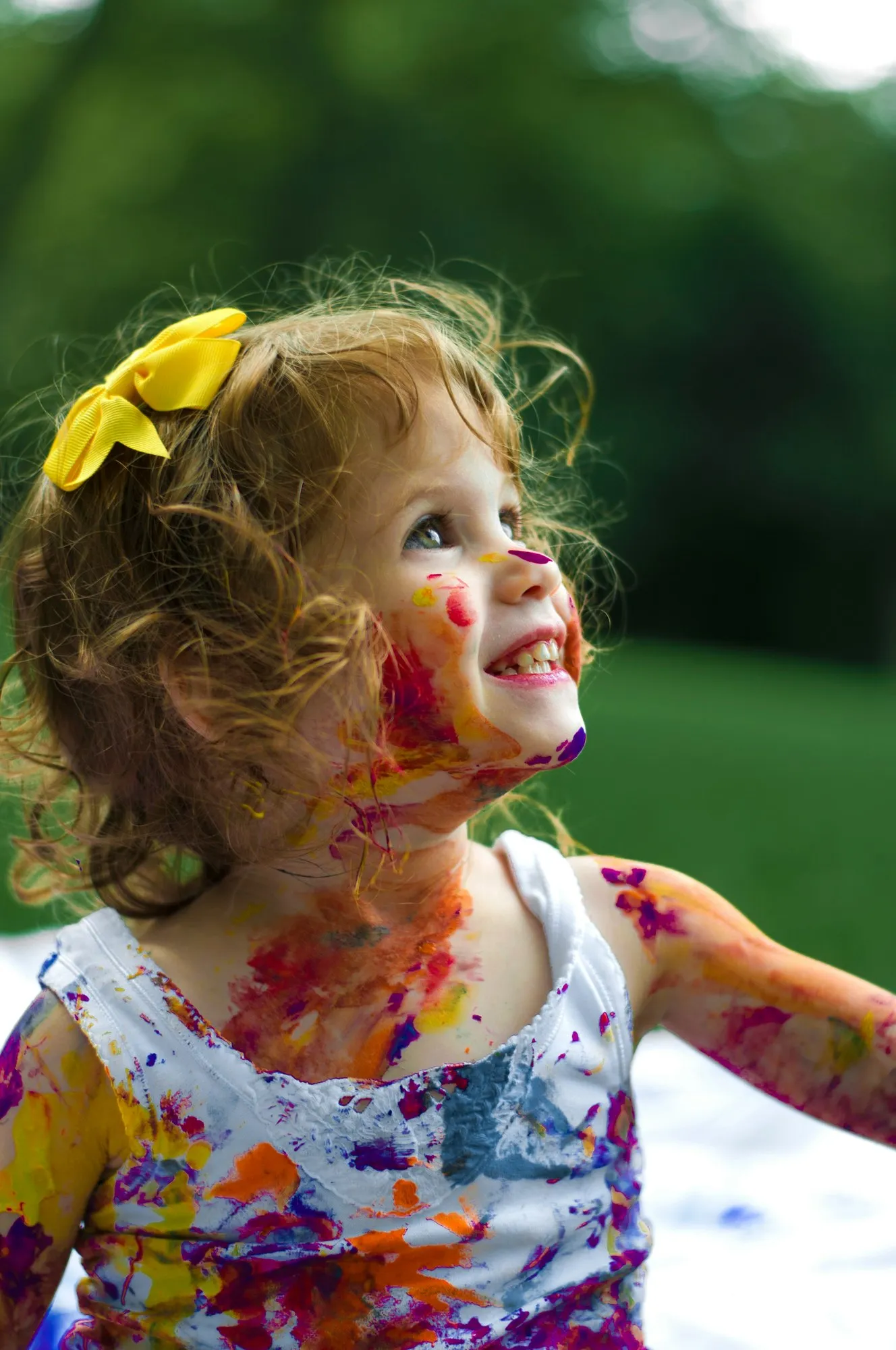 A toddler outdoors with paint on their hands and face, laughing